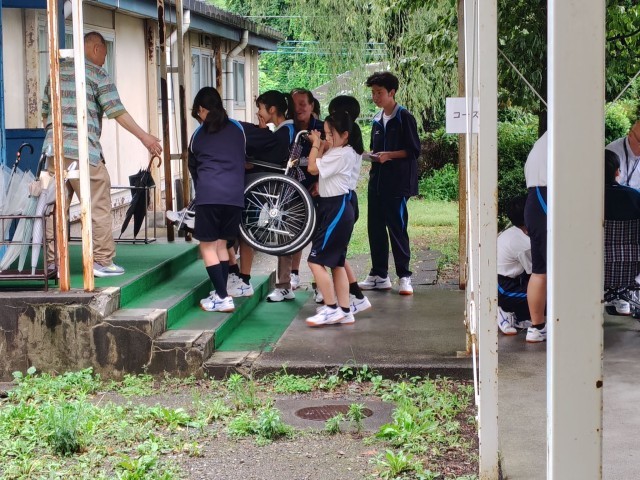 車いすを４人で運ぶ